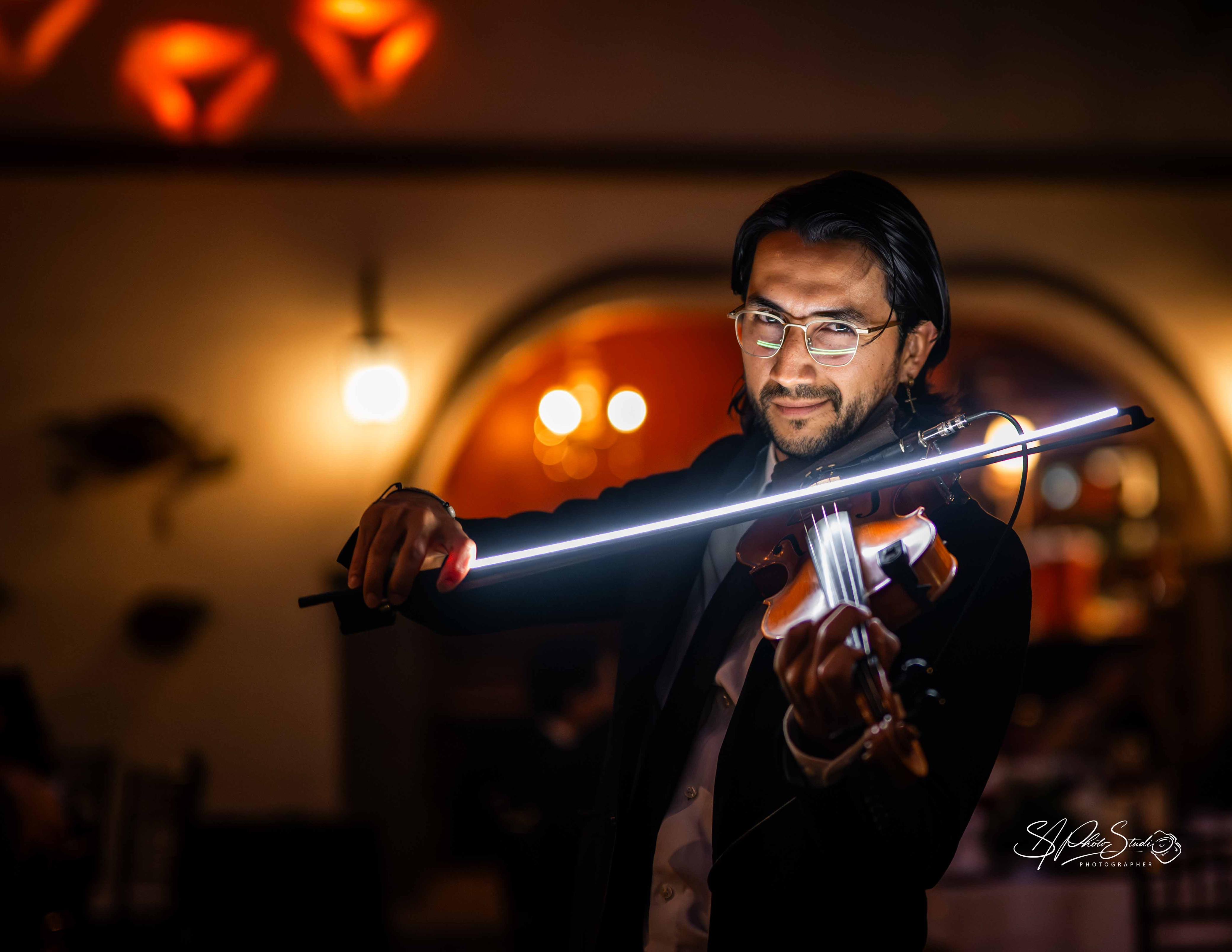 Yael Magaña tocando violín con arco luminoso en una boda, con invitados alrededor